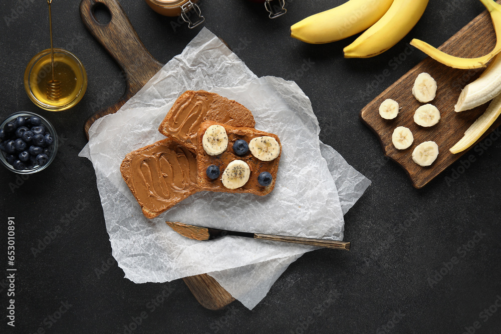 Baking paper of toasts with peanut butter, fresh fruits and honey on black background