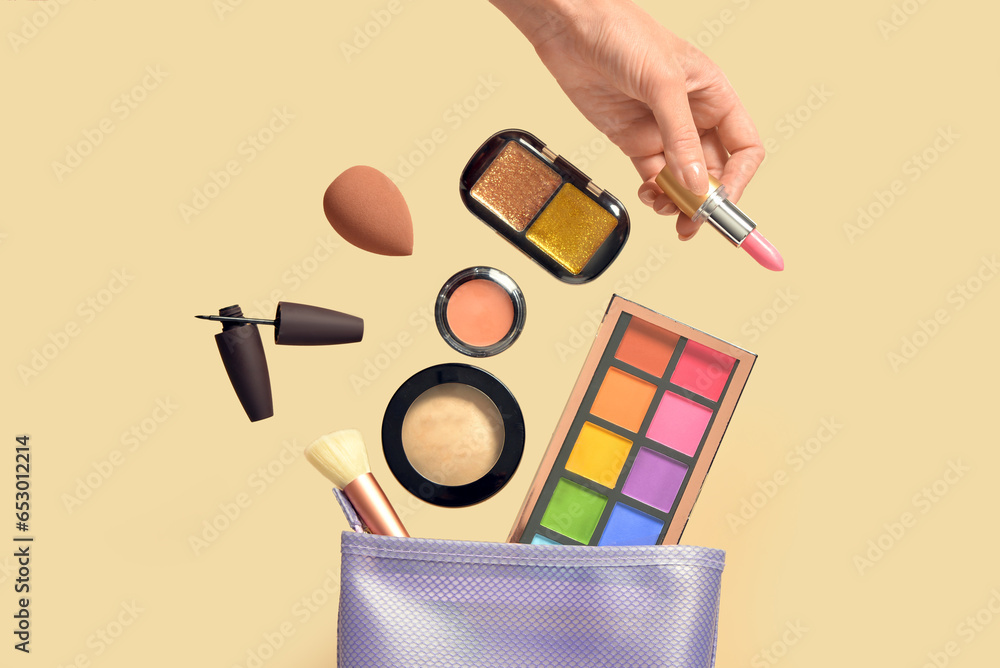 Woman holding lipstick and cosmetic bag with different makeup products on yellow background