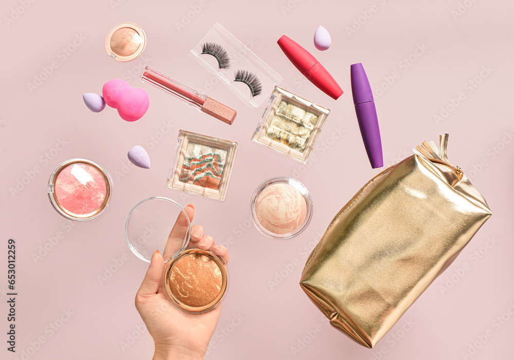 Woman holding highlighter and cosmetic bag with different makeup products on lilac background