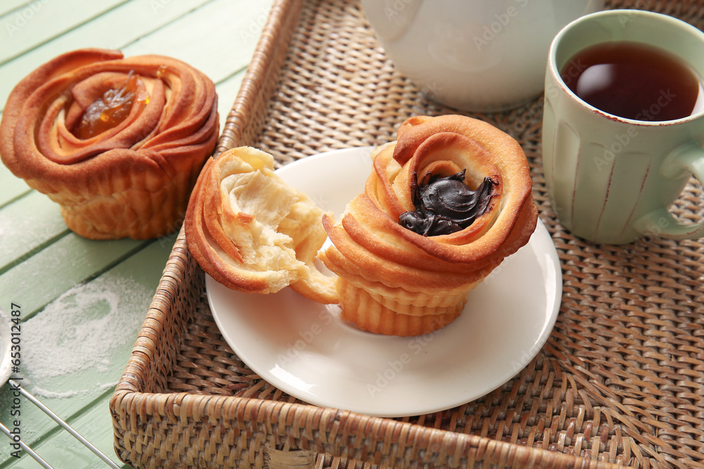 Tray with tasty cruffins and cup of tea on green wooden background