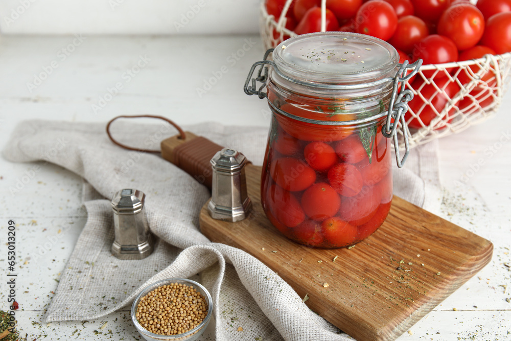 Wooden board with jar of pickled tomatoes on white background