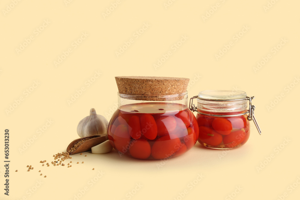 Jars of pickled tomatoes with different spices on yellow background