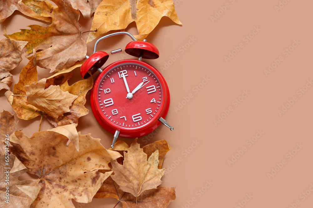 Alarm clock with autumn leaves on brown background