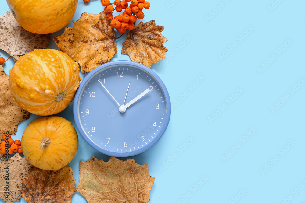 Alarm clock with autumn leaves and pumpkins on blue background