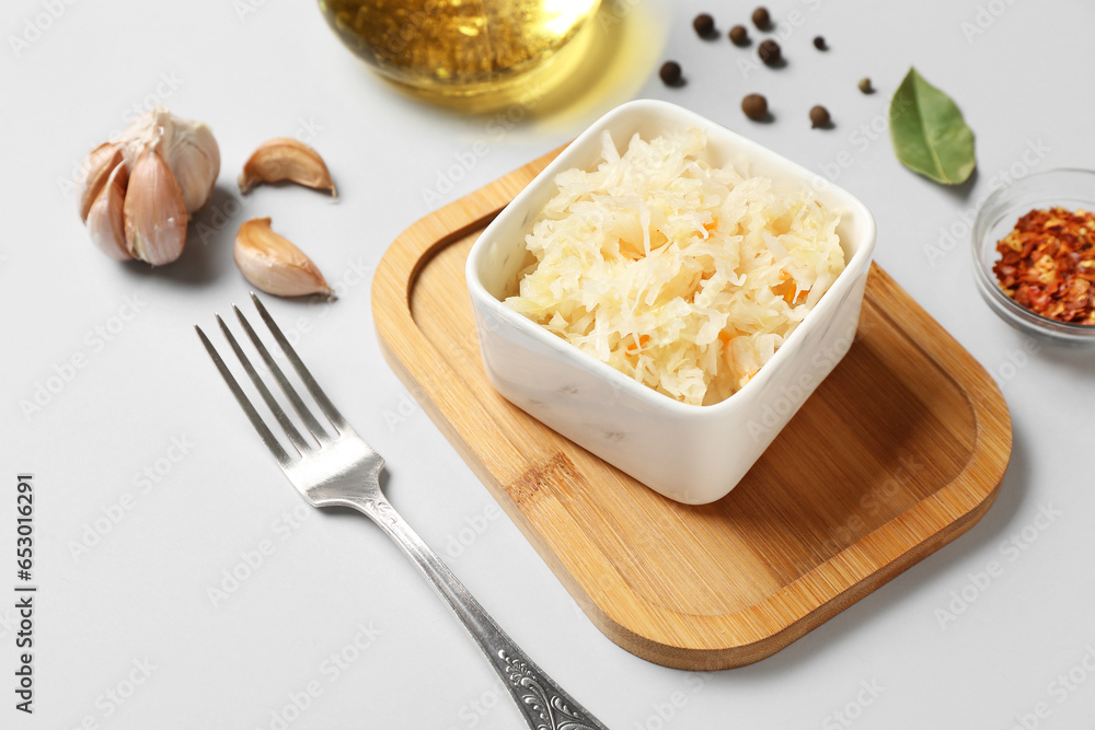 Board with bowl of tasty sauerkraut and ingredients on white background