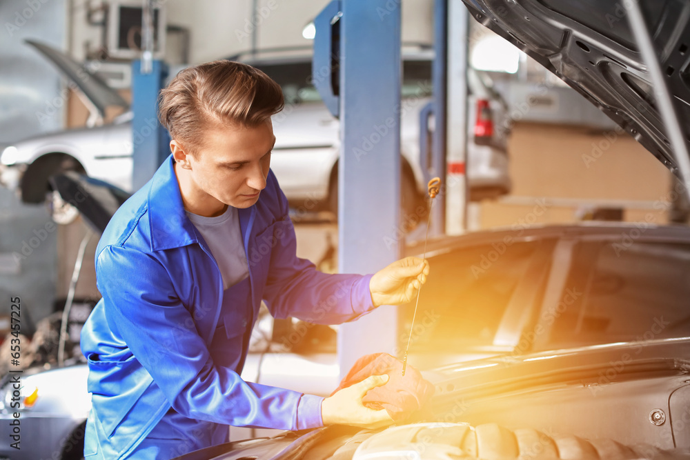 Male mechanic checking engine oil level in car service center