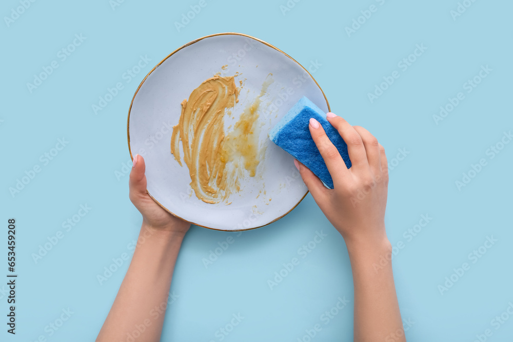 Female hands washing dirty plate with sponge on blue background