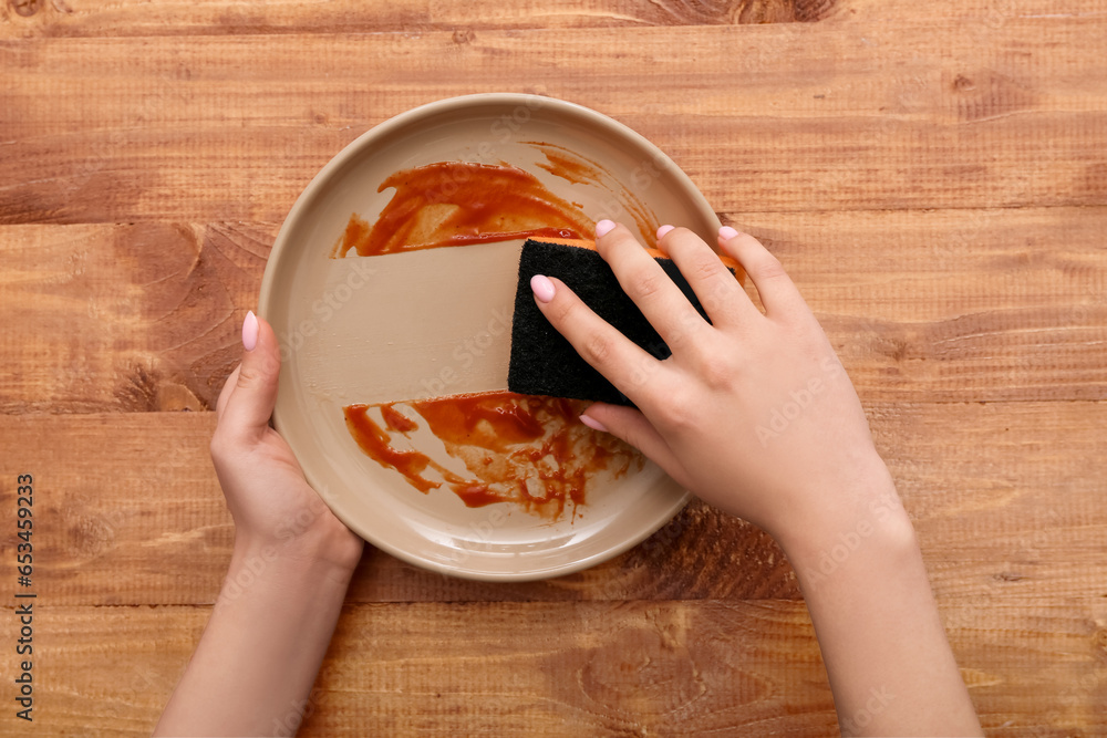 Female hands washing dirty plate with sponge on wooden background