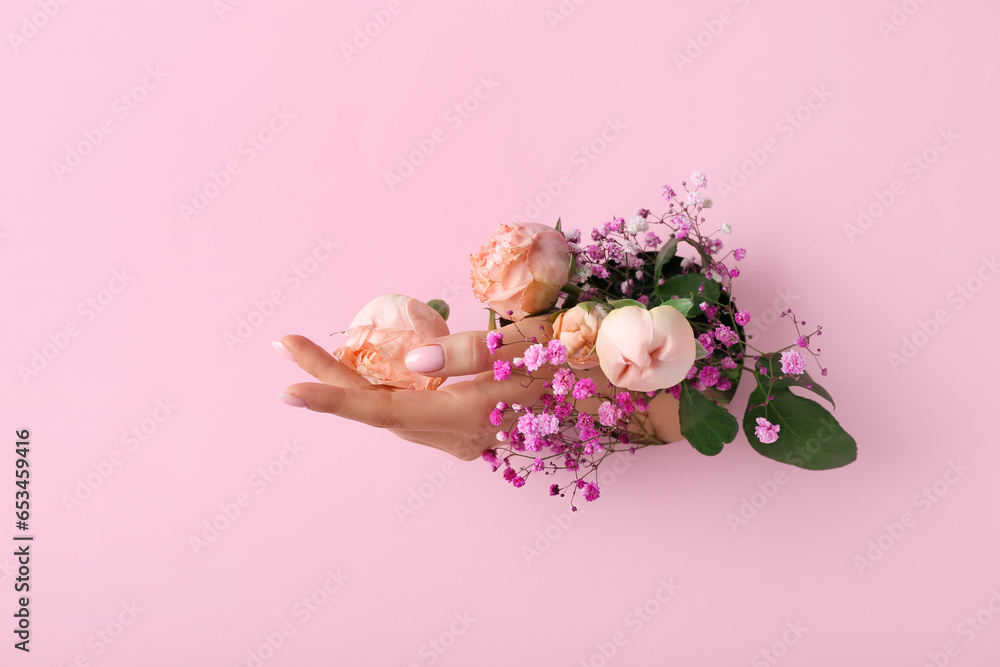 Female hand with flowers visible through hole in pink paper