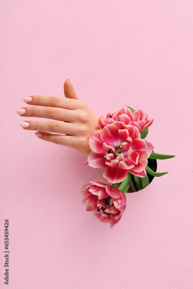 Female hand with tulips visible through hole in pink paper