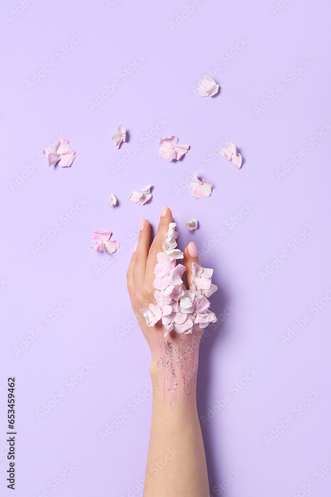 Woman with glitter and floral petals on lilac background. Hand care concept