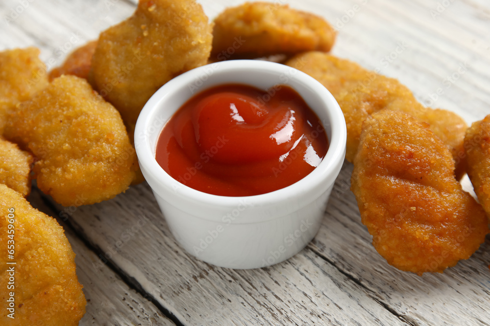 Delicious nuggets and bowl with ketchup on white wooden table, closeup