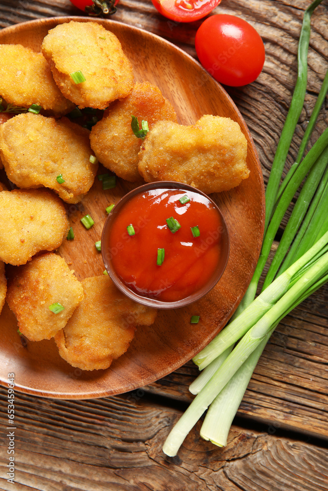 Plate with delicious nuggets, bowl of ketchup and vegetables on wooden table, closeup