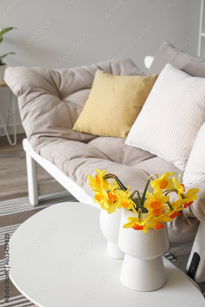 Vase with blooming narcissus flowers on coffee table in living room