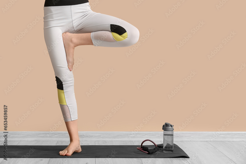 Sporty woman doing yoga on mat near beige wall in gym