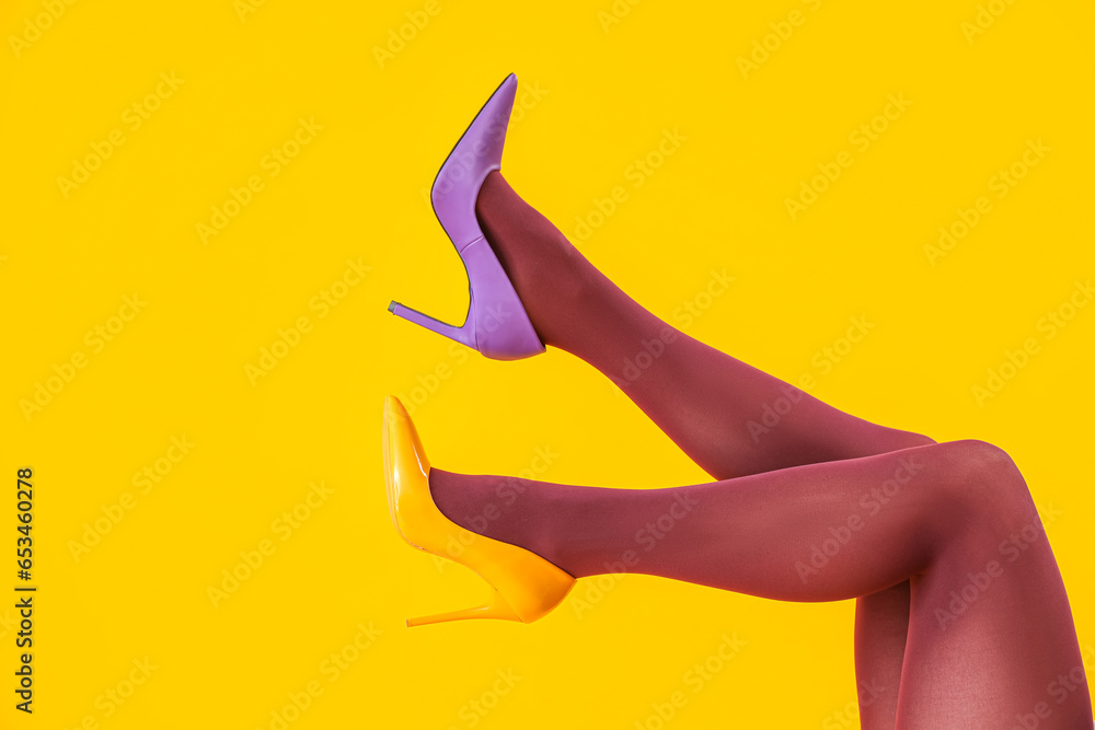 Female legs in black tights and different heels on yellow background