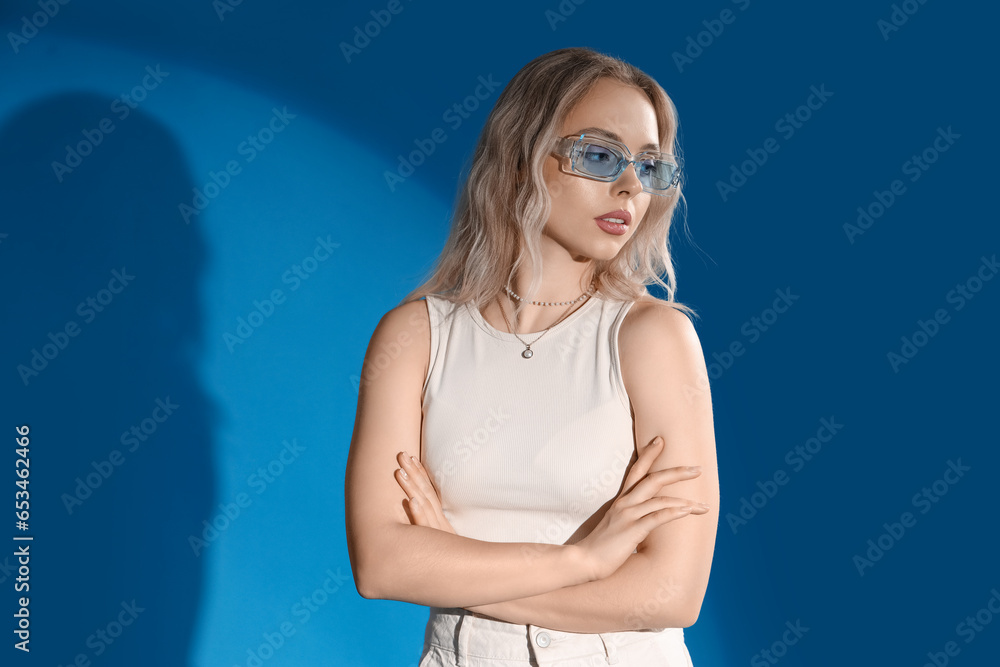 Young woman in stylish sunglasses on blue background