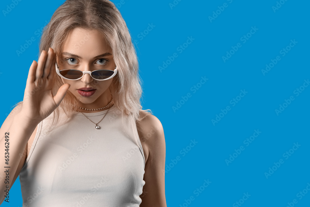 Young woman in stylish sunglasses on blue background, closeup