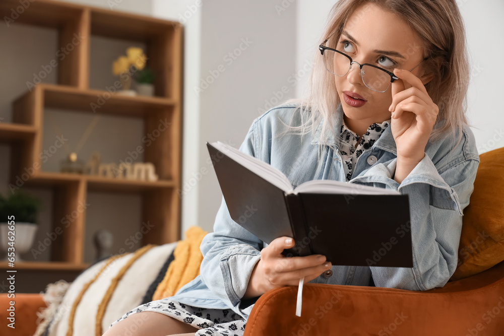 Young woman in stylish eyeglasses reading book at home, closeup