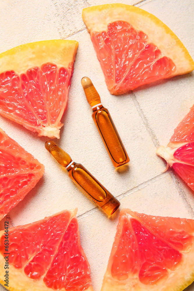 Ampoules with vitamin C and grapefruit slices on white tile background