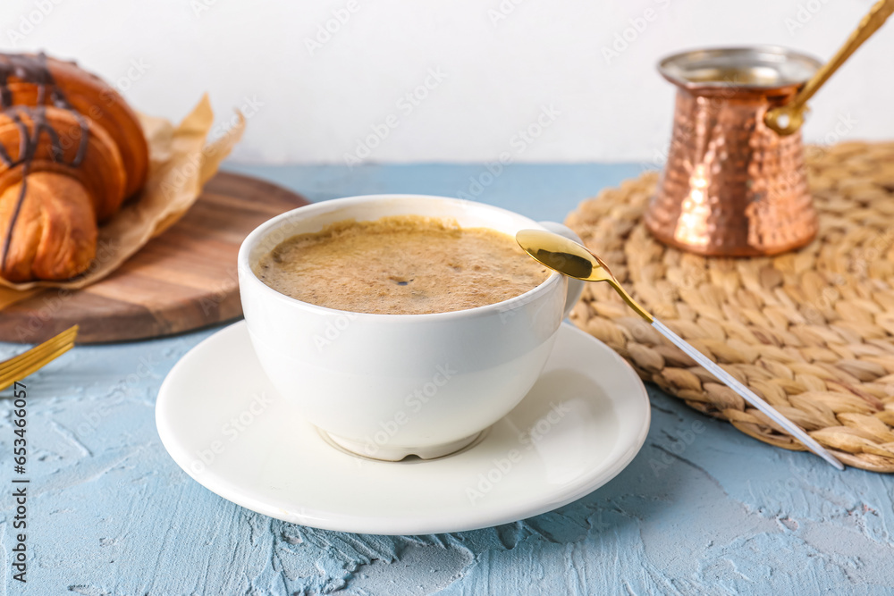 Cup of delicious espresso with jezve and croissant on blue background