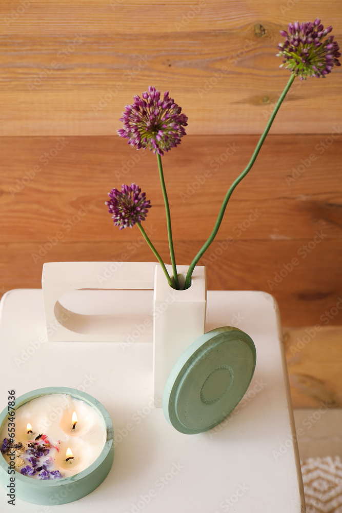 Beautiful flowers and candle on chair near wooden wall in room, closeup