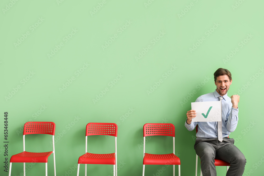 Happy male applicant holding paper sheet with check mark in room