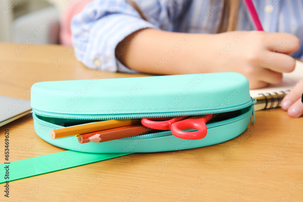 Little girl with pencil case drawing at table, closeup