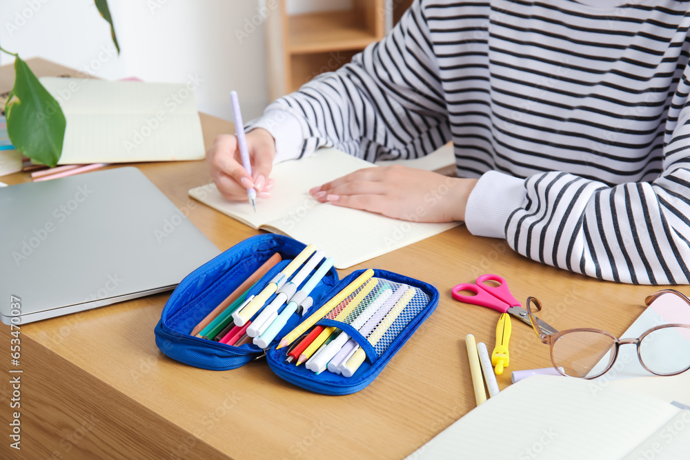 Female student with pencil case writing in copybook at table, closeup