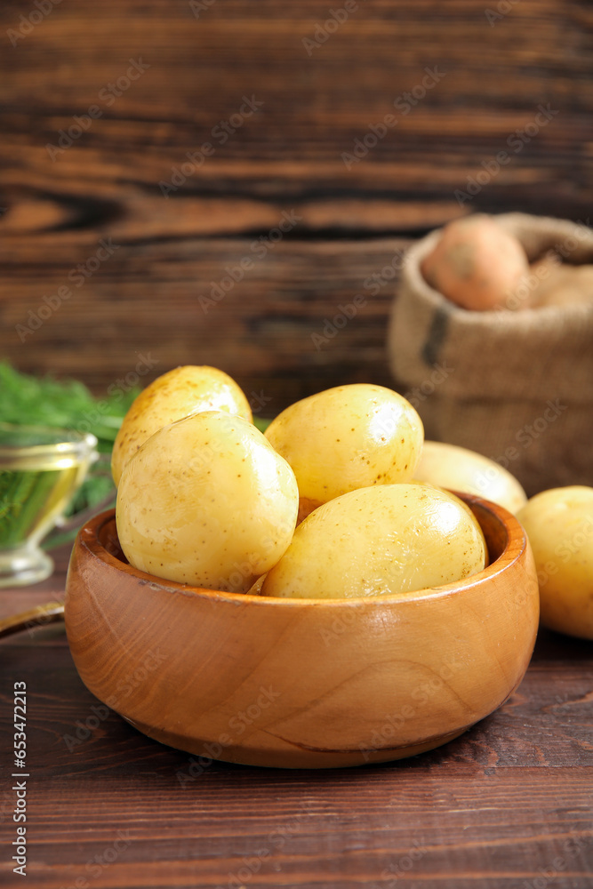 Bowl with raw potatoes on wooden background