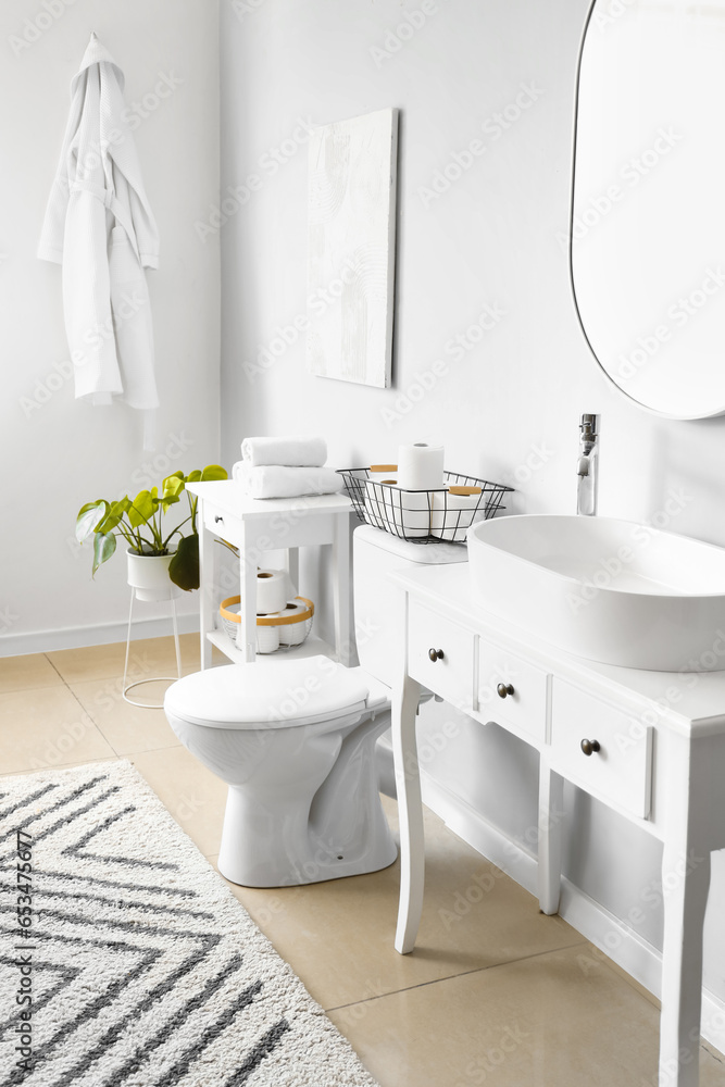 Interior of light restroom with ceramic toilet bowl and vanities