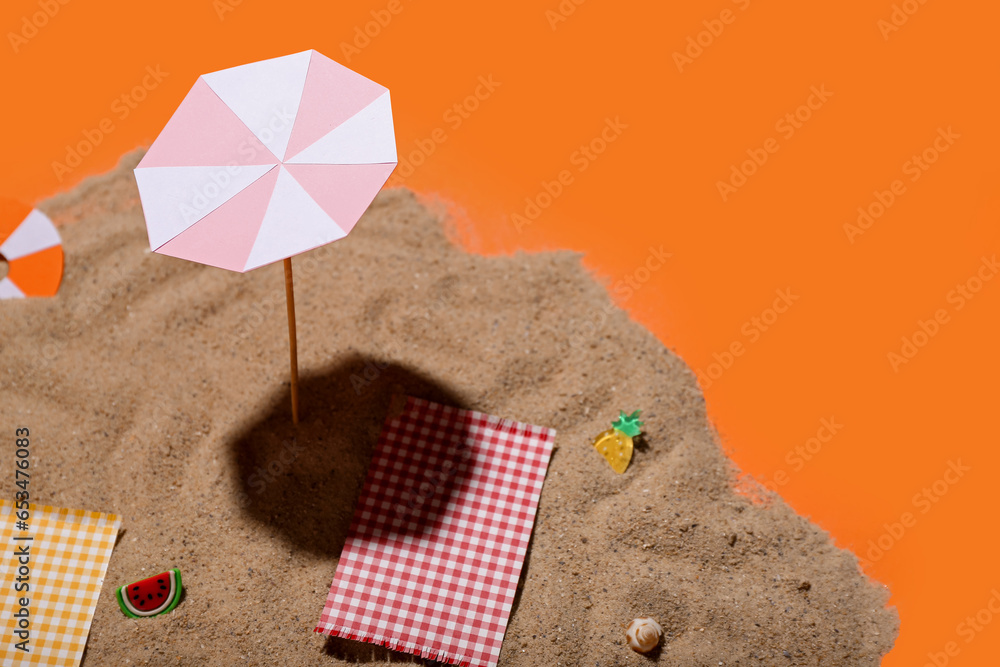 Creative summer composition with mini umbrella, beach accessories and sand on orange background