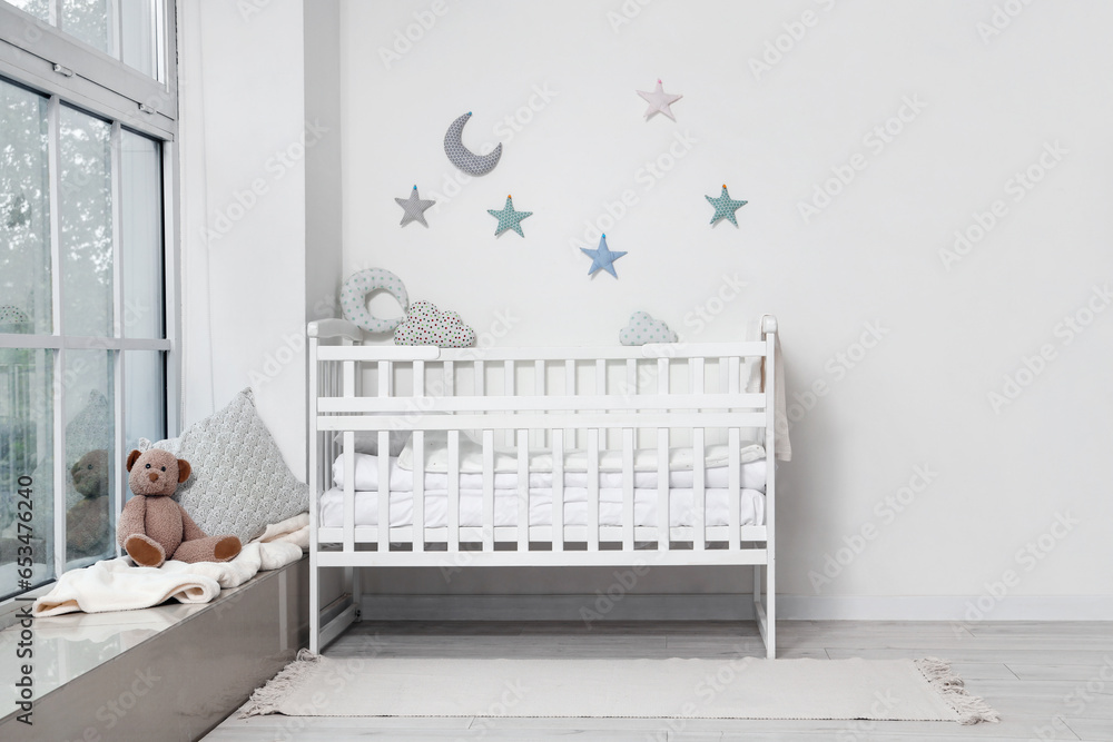 Interior of childrens room with crib and teddy bear near window