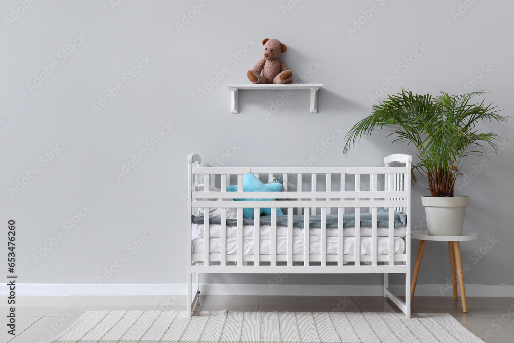 Interior of childrens room with crib and teddy bear on shelf near white wall