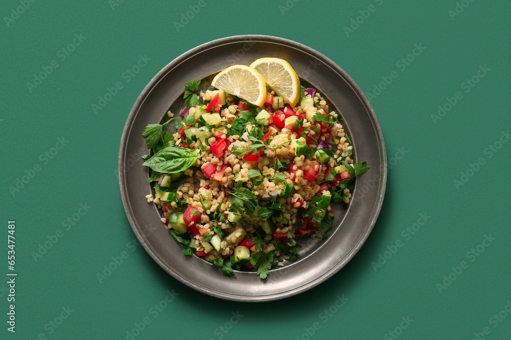 Plate with delicious tabbouleh salad and lemon slices on green background