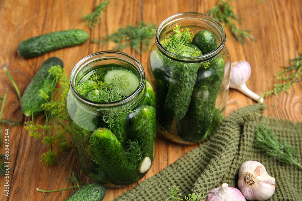 Jars with fresh cucumbers and ingredients for canning on wooden background