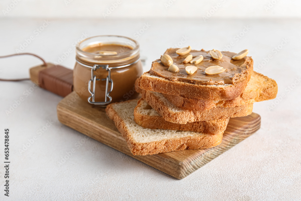 Wooden board of toasts with peanut butter and nuts on white background