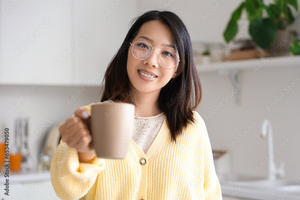 Beautiful young Asian woman with cup of tasty tea at kitchen