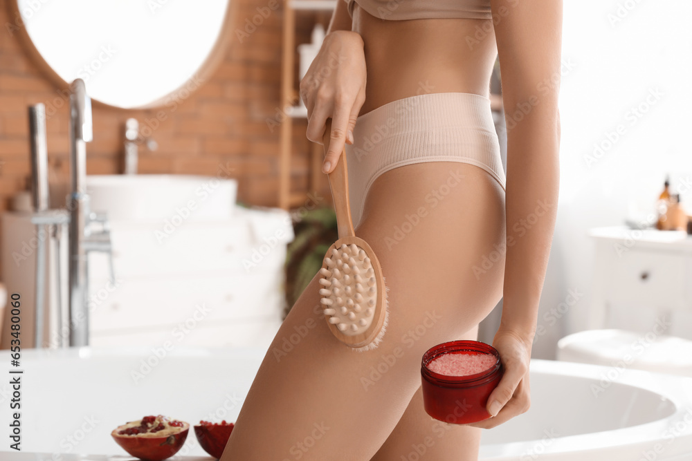 Young woman with pomegranate scrub and massage brush in bathroom, closeup