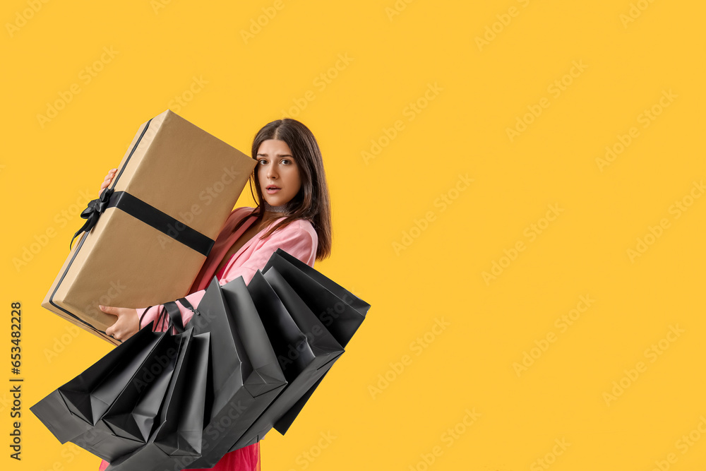 Young woman with gift and shopping bags on yellow background. Black Friday sale