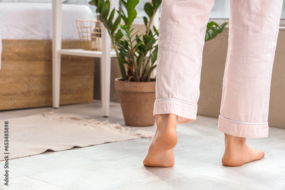 Barefoot woman walking on floor with heating in bedroom, back view