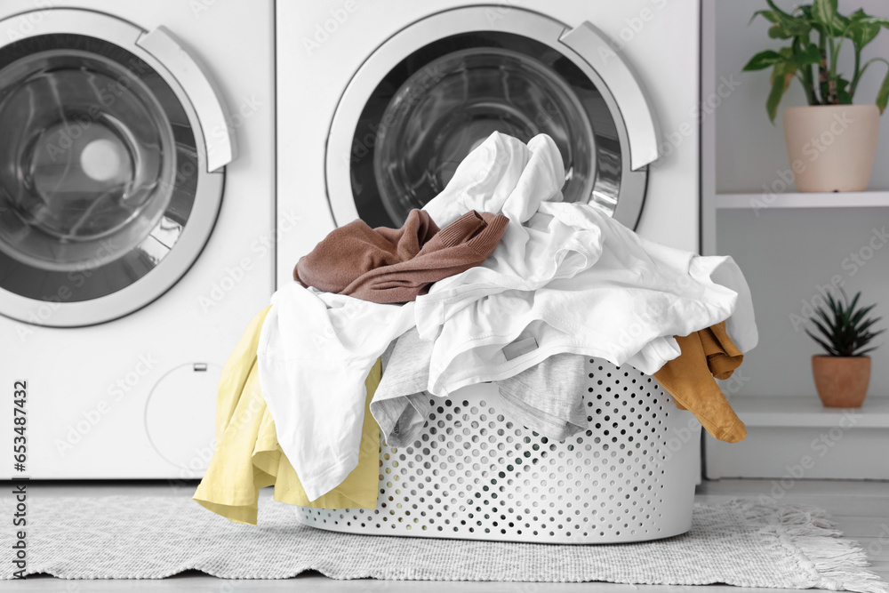 Basket with dirty clothes near washing machines in laundry room