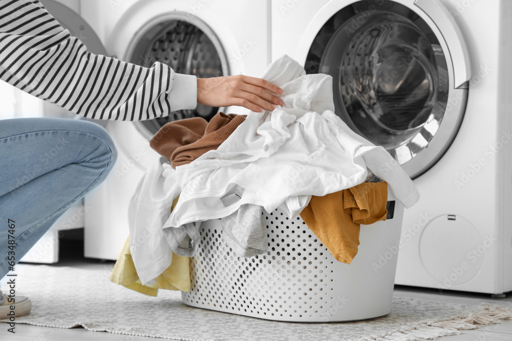 Young woman putting dirty clothes into washing machine in laundry room, closeup