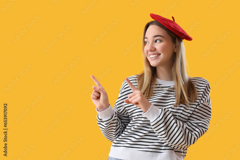 Young woman pointing at something on yellow background