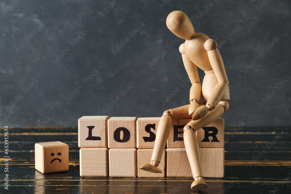 Wooden cubes with word LOSER and mannequin on table near dark wall