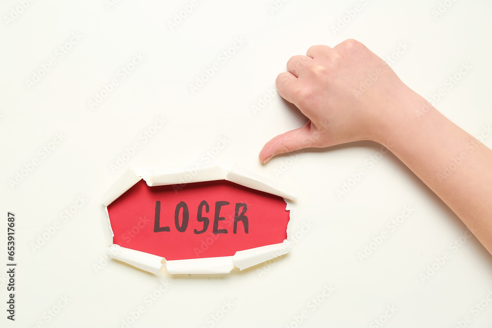 Woman showing thumb-down and word LOSER visible through hole in white paper