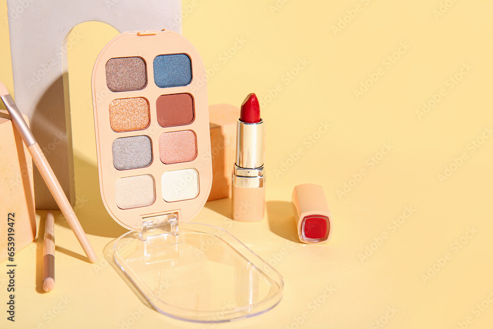 Palette of eyeshadows, lipstick, makeup brushes and plaster podiums on color background