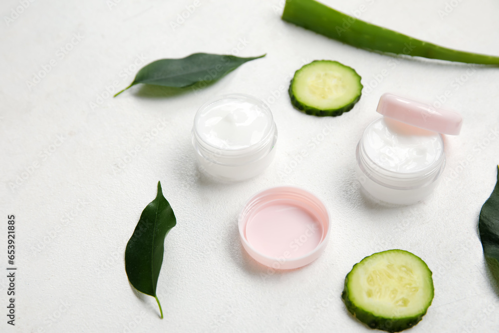 Composition with jars of natural cream, ingredients and plant leaves on light background