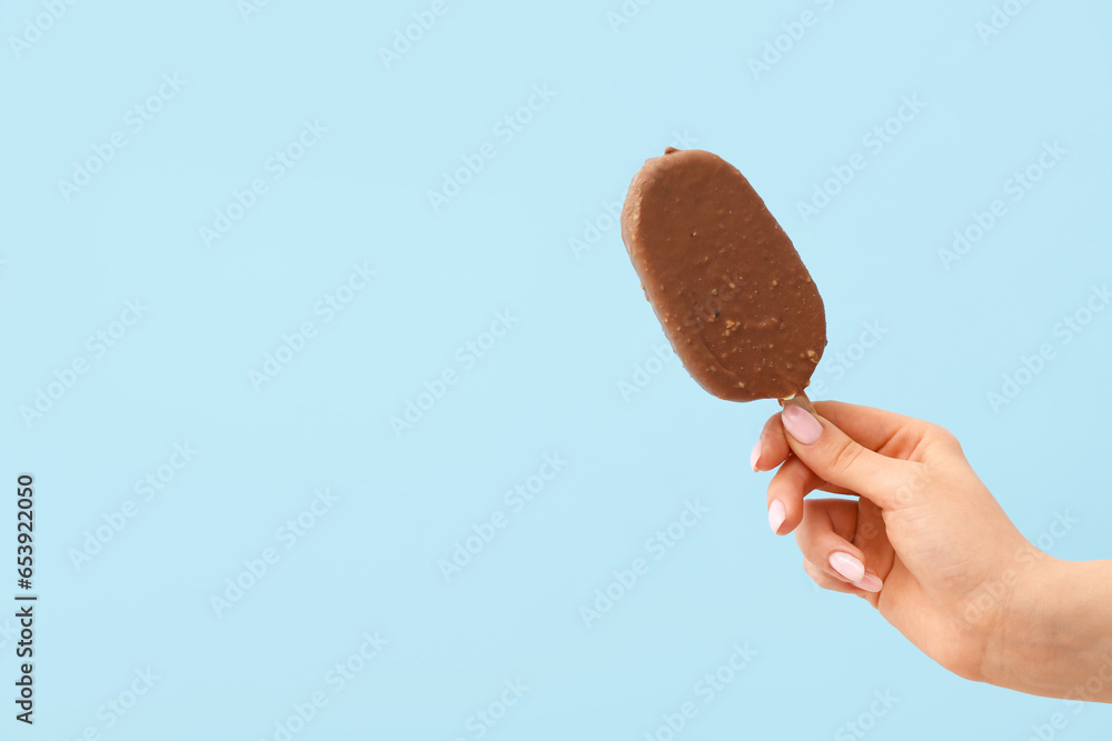 Woman holding delicious chocolate covered ice cream on stick against blue background