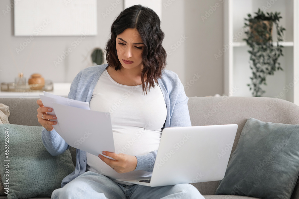 Young pregnant woman working with documents and laptop at home